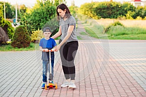 Mother helping son to learn riding the scooter. Active kids leisure