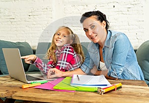 Mother helping young girl doing homework with laptop and school books sitting on the sofa at home in parenting homework and