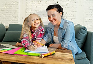 Mother helping young girl doing homework with laptop and school books sitting on the sofa at home in parenting homework and