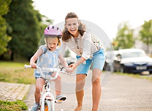 A mother helps her daughter learns to ride a bike