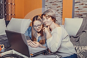 Mother helps her teenage daughter with homework, while are they together browsing internet on smartphone