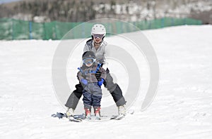 Mother Helps Toddler Boy Ski Downhill. Dressed Safely with Helmet