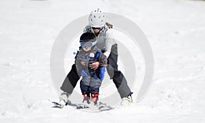 Mother Helps Toddler Boy Ski Downhill. Dressed Safely with Helmets