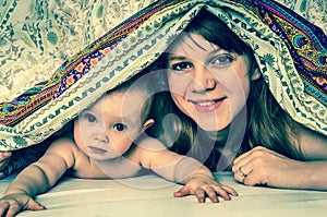 Mother and her baby playing and smiling under a blanket