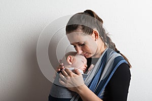 Mother with her baby son sleeping in sling. Studio shot.