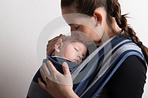 Mother with her baby son sleeping in sling. Studio shot.