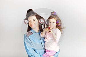 Mother and her child daughter with a lipstick. Portrait of a lovely little baby girl and her mum with curlers on their heads