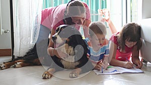 A mother with her child are drawing at home meanwhile they pamper the family dog