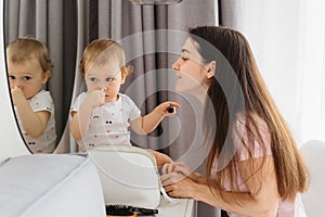 Mother and her child girl are doing makeup and having fun near mirror