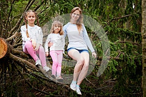 Mother and her child sister girls playing and having fun together on walk in forest outdoors. Happy loving family posing on nature