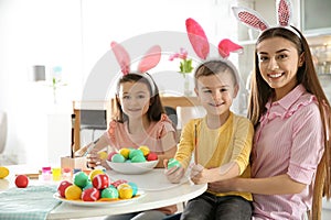 Mother and her children with bunny ears headbands painting Easter eggs in kitchen