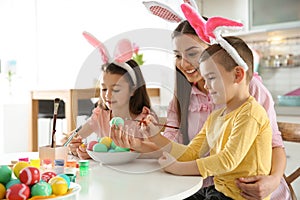 Mother and her children with bunny ears headbands painting Easter eggs in kitchen