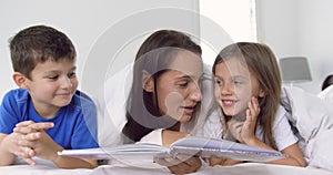 Mother with her children reading story book in bedroom at home 4k