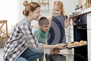 Mother and her children taking out cookies from oven
