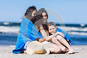 Mother and her children wrapped in a blanket by the sea.