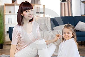 Mother and her cute little baby girl in towel after bath, sitting on the floor in modern appartment interior indoors