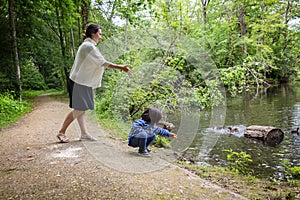 Mother and her cute little child feeding ducks in the pond in a park