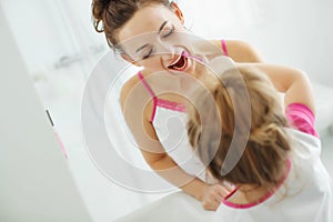 Mother and her daughter brush their teeth with toothbrushes in the bathroom at home. Mom and baby girl in home clothes.