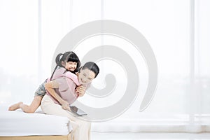 Mother and her daughter child girl playing and hugging on bed in bedroom