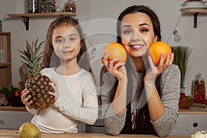 Mother and her daughter are doing a fruit cutting and having fun at the kitchen.