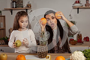 Mother and her daughter are doing a fruit cutting and having fun at the kitchen.