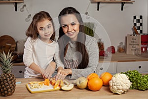 Mother and her daughter are doing a fruit cutting and having fun at the kitchen.