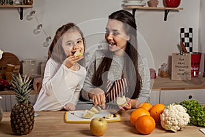 Mother and her daughter are doing a fruit cutting and having fun at the kitchen.