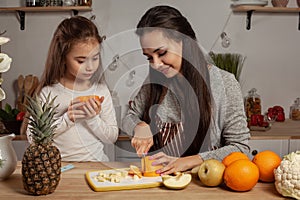 Mother and her daughter are doing a fruit cutting and having fun at the kitchen.