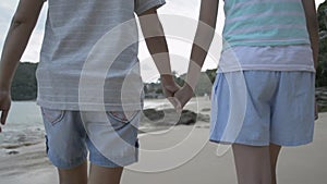 Mother and her daughter are holding hands together and walking leisurely on the beach in the evening.