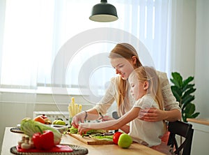 Mother with her daughter in kitchen preparing healthy food with fresh vegetables