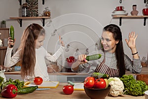 Mother and her daughter are making a vegetable salad and having fun at the kitchen.