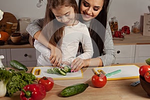 Mother and her daughter are making a vegetable salad and having fun at the kitchen.