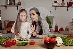 Mother and her daughter are making a vegetable salad and having fun at the kitchen.