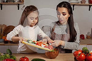 Mother and her daughter are making a vegetable salad and having fun at the kitchen.
