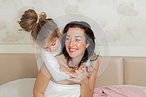 Mother and her daughter playing and hugging in the bed. Happy loving family.