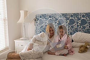 Mother with her daughter reading storybook in bedroom