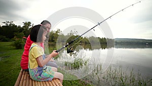 Mother with her daughter side by while fishing at lake. Concept of connecting children with nature.