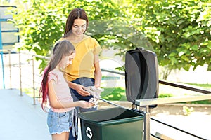 Mother and her daughter throwing paper into recycling bin