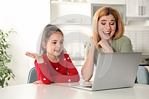 Mother and her daughter using video chat on laptop at table