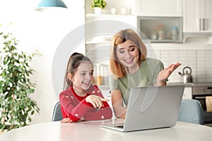 Mother and her daughter using video chat on laptop at table