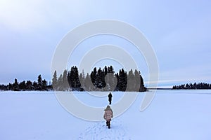A mother and her daughter walking along the frozen Astotin Lake on a snowy winter day admiring the view at Elk Island Park