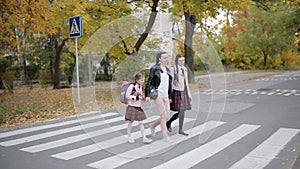 Mother with her daughters are going to school cross the road at a pedestrian crossing.