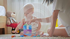 Mother and her kid play with toys indoors. Crawling funny baby boy on floor at home. Mother and little son playing with