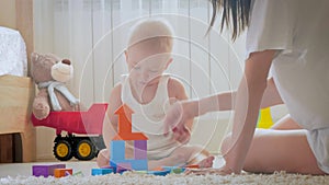 Mother and her kid play with toys indoors. Crawling funny baby boy on floor at home. Mother and little son playing with