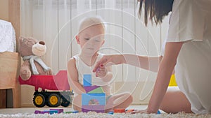 Mother and her kid play with toys indoors. Crawling funny baby boy on floor at home. Mother and little son playing with