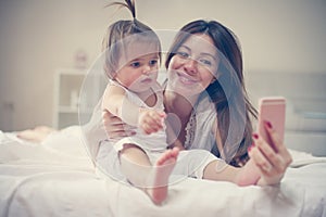 Mother with her little baby having fun in the bed.