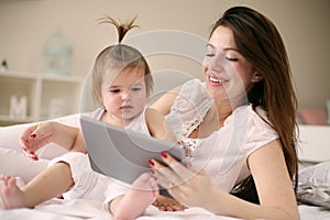 Mother and her little baby at home. Mother with her baby watching something on digital tablet.