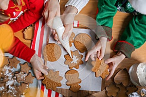 Mother and her little children decorating tasty Christmas cookies at wooden table, top view