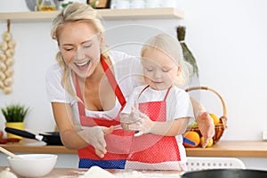 Mother and her little daughter cooking holiday pie or cookies for Mother`s day. Concept of happy family in the kitchen