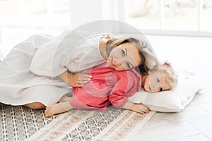 Mother and her little daughter are lying on a pillow on the floor, spending their free time together